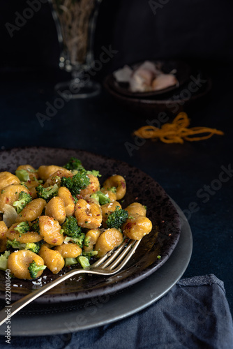italian food: orange pumpkin gnocchi seasoned with broccoli, hot pepper and ricotta. Dark image 
