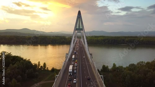 Budapest, Hungary - 4K flying above Megyeri Bridge at sunset with heavy afternoon traffic with golden sky and Buda Hills at background