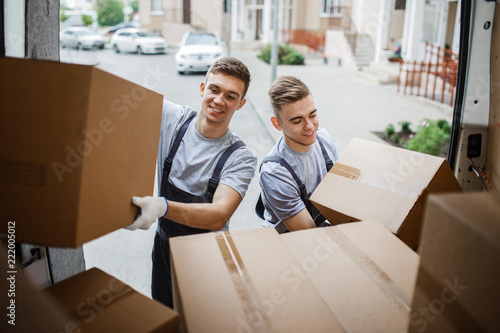 Two young handsome smiling movers wearing uniforms are unloading
