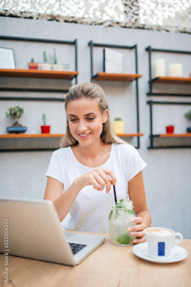 Yooung woman at cafe drinking lemonade and working on laptop.