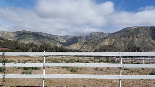 Dry pasture enclosed in a white wooden fence, and backed by coastal mountains.