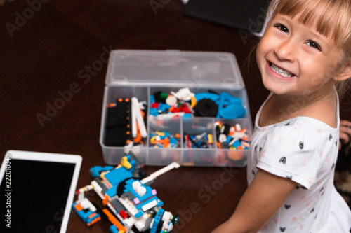 Cute little girl is playing with robot at home and programming it on tablet. STEM education. 