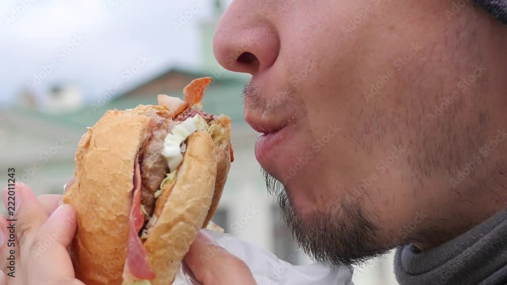 Closeup hunger man eating bites and chews a big burger with cutlet and bacon Closeup hunger man eating bites and chews a big burger with cutlet and bacon