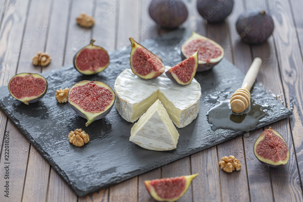 Brie cheese with fresh figs, honey and nuts. On shale plate and wooden background.