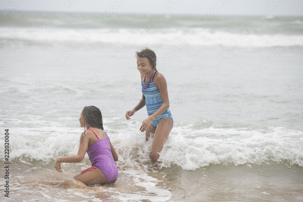 Two mixed-race sisters playing and laughing having fun on the beach on a bright tropical summer holiday Two mixed-race sisters playing and laughing having fun on the beach on a bright tropical summer holiday