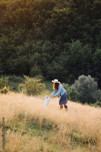 girl in a hat playing with a dog in the field at sunset sun