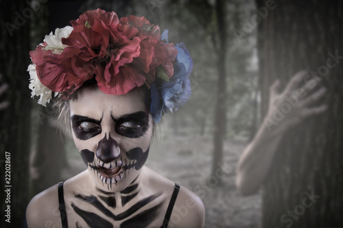 Curly hair girl with sugar skull Catrina Calavera make up and red rose natural flowers headband close up. Day of Dead. Dia de Los Muertos