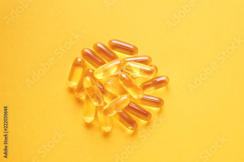 Bunch of omega 3 fish liver oil capsules forming circle shaped pattern. Close up of big golden pills texture. Healthy every day nutritional supplement. Top view flat lay, copy space, yellow background