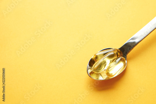 Bunch of omega 3 fish liver oil capsules in silver spoon. Close up of big golden translucent pills in pile. Healthy every day fatty acids nutritional supplement dosage. Top view, flat lay, copy space. photo