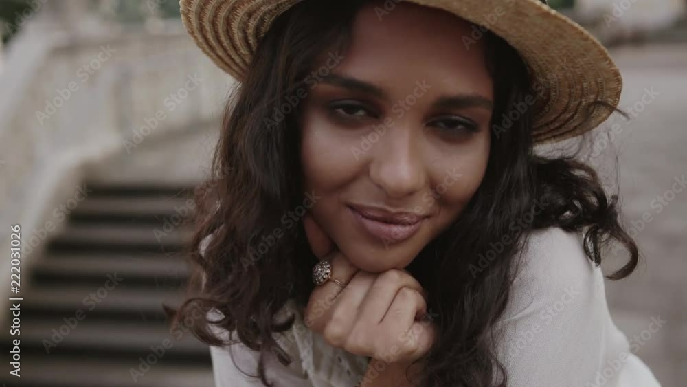 Close up view of pretty curly woman in a trendy summer straw hat seductively looking straight to camera and charmingly smiling. Female beauty, cheerful mood, positive emotions. Female portrait Close up view of pretty curly woman in a trendy summer straw hat seductively looking straight to camera and charmingly smiling. Female beauty, cheerful mood, positive emotions. Female portrait
