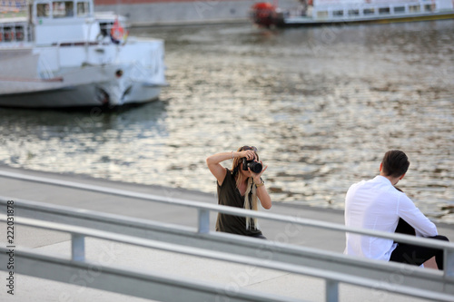 Kobieta fotograf robi zdjęcia parze młodych ludzi w plenerze nad rzeką.
