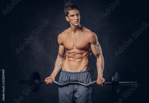 Handsome shirtless man with stylish hair and muscular ectomorph doing the exercises with the barbell.