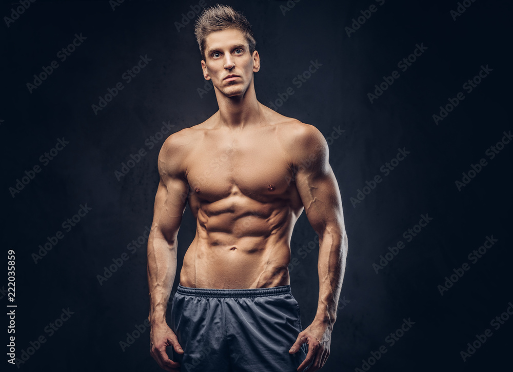 Handsome shirtless ectomorph bodybuilder with stylish hair posing on a dark background.