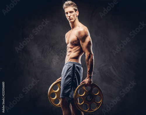 Handsome shirtless ectomorph bodybuilder with stylish hair posing with a barbell disk on dark background. photo