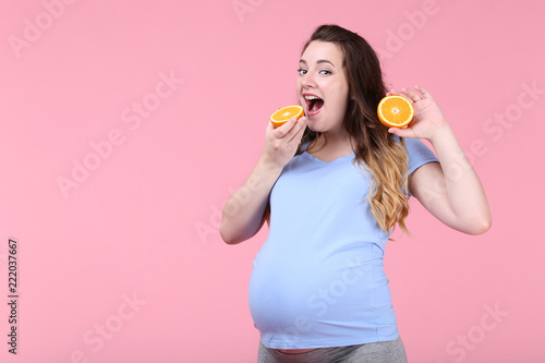 Beautiful pregnant woman with orange fruit on pink background