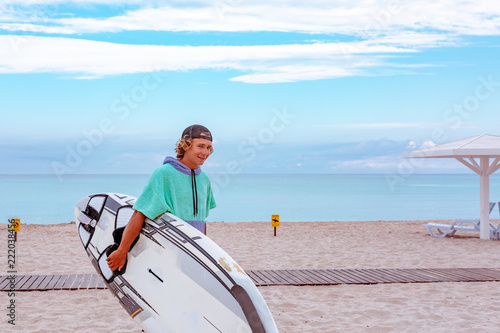 Handsome man walk with white blank surfing board wait for wave to surf spot at sea ocean shore. View from side. Concept of sport, fitness, freedom, happiness, new modern life, hipster.