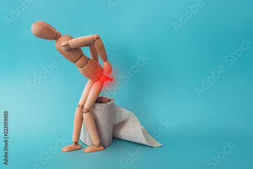 Wooden figure sit on a roll of toilet paper. Concept of the problem with hemorrhoids.