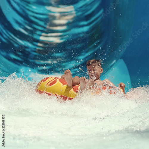 Boy having fun on the water slide in the aqua fun park. Happy falling into water and water splashes are all over.