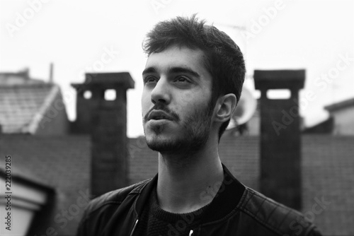 Black and white close portrait of a young light bearded spanish man on the roofs of a city