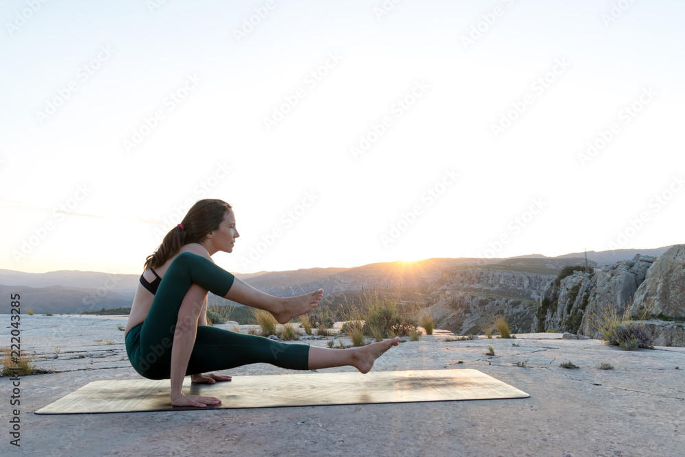 Woman practicing yoga on mountain top during sunset