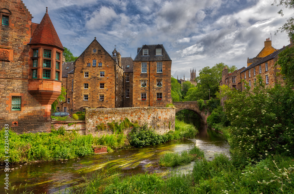Quaint stream with green flora along it flowing through Dean Village in Edinburgh with old Scottish buildings