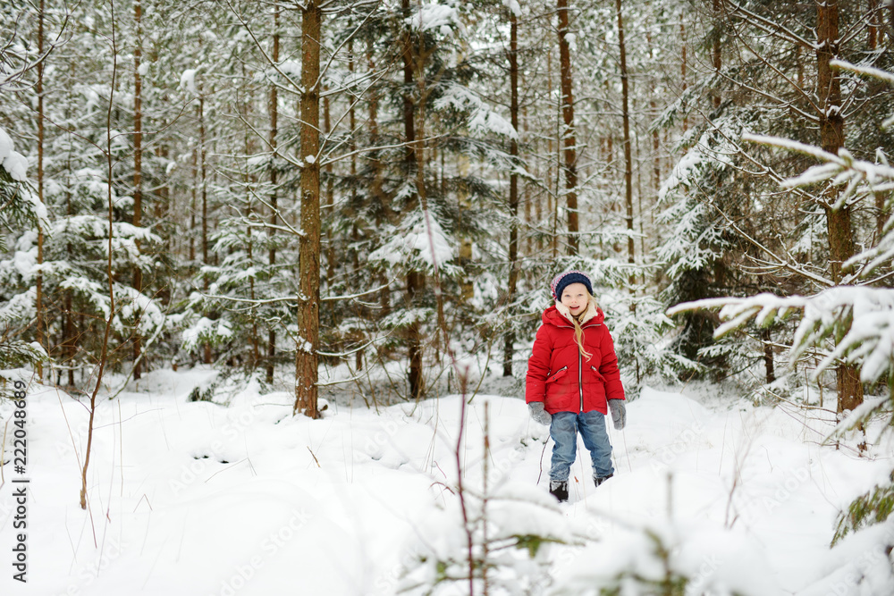 Adorable little girl having fun in beautiful winter forest. Happy child playing in a snow.