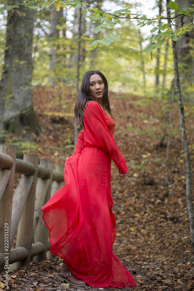 Black haired and green eyed woman in red dress in the forest. Black haired and green eyed woman in red dress in the forest.
