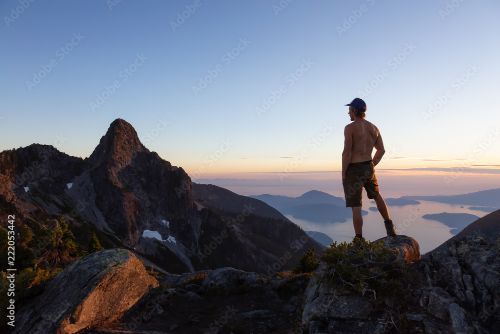 Man on top of a mountain enjoying the beautiful view during a vibrant summer sunset. Taken in Howe Sound, near Vancouver, BC, Canada.