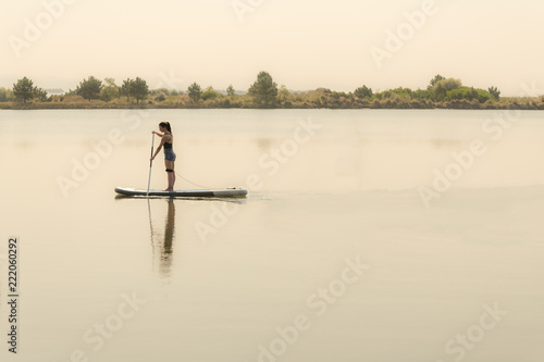 Woman stand up paddleboarding on lake. Young girl doing watersport on lake. Female tourist in swimwear during summer vacation.