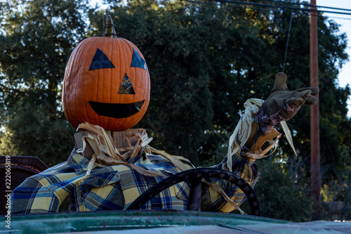 Smiling, happy, welcoming, fun friendly pumpkin head scarecrow driving an old truck to a halloween harvest party