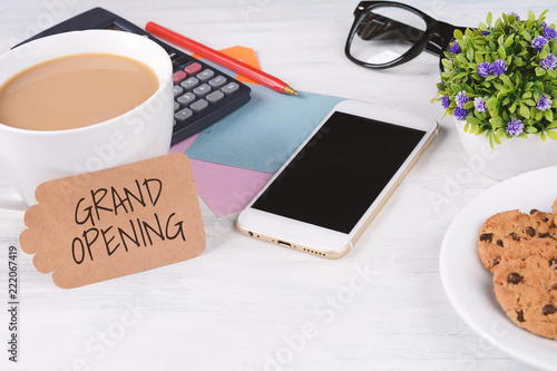Paper card with "grand opening" text and coffee with phone, calculator, cookies and glasses