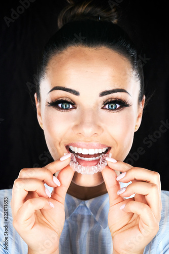 Stomatology concept, head and shoulders of woman with strong white teeth looking at camera and smiling, holding false tooth, denture. Young woman at dentist's, Invisalign orthodontics