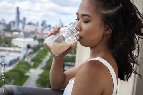 Young Asian woman enjoying a relaxing evening on the balcony with her coffee with the beautiful Chicago skyline in the background. wearing a white tank top looking into the distance