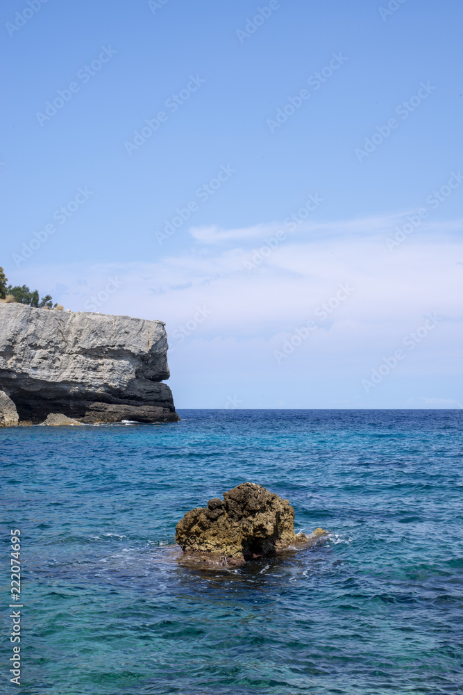 Rock in Middle of Sea with Cliff and Sky in Background