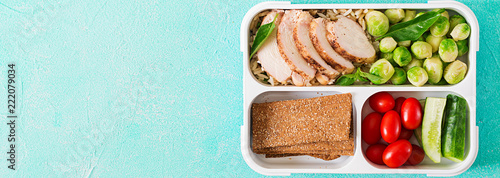 Healthy green meal prep containers with chicken fillet, rice, brussels sprouts and vegetables overhead shot with copy space. Dinner in lunch box. Banner. Top view. Flat lay