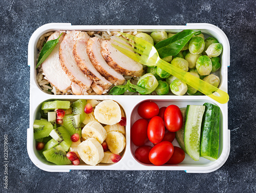 Healthy green meal prep containers with chicken fillet, rice, brussels sprouts, vegetables and fruits overhead shot with copy space. Dinner in lunch box. Top view. Flat lay