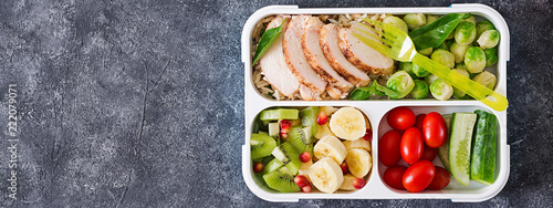 Healthy green meal prep containers with chicken fillet, rice, brussels sprouts, vegetables and fruits overhead shot with copy space. Dinner in lunch box. Top view. Banner. Flat lay