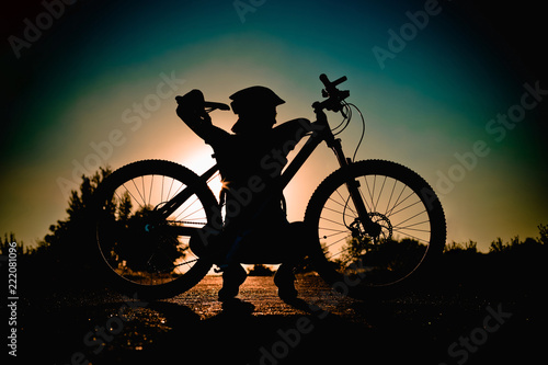 Silhouette of a girl with a bicycle at sunset in the summer