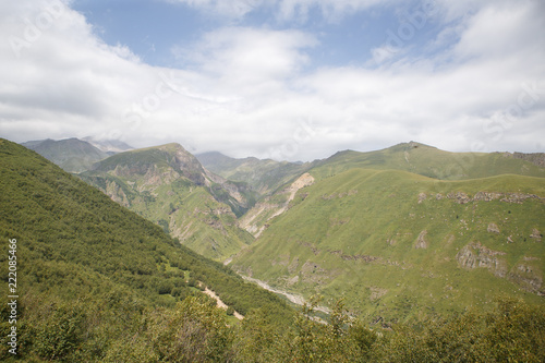 Mountain gorge of Georgia, top view of the green hills with a cleft on the Georgian military road. The sky is covered with cloudy grey clouds, the gorge is in fog.