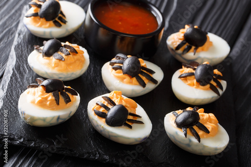 Halves devilish eggs decorated with olive spiders close-up served with ketchup. Halloween food. horizontal