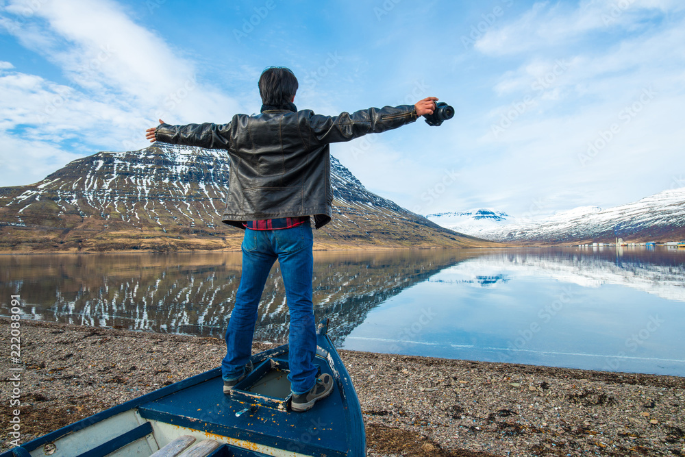 Naklejka premium Happy man standing on the old boat and looking to the beautiful view of Holmatindur mountain in Eskifjordur town of East region of Iceland 