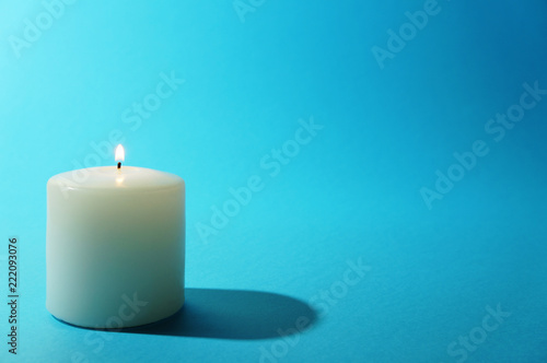 White candle burning on blue backgound photo