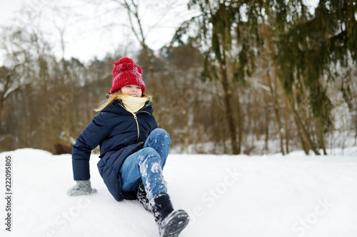 Adorable little girl having fun in beautiful winter forest. Happy child playing in a snow.