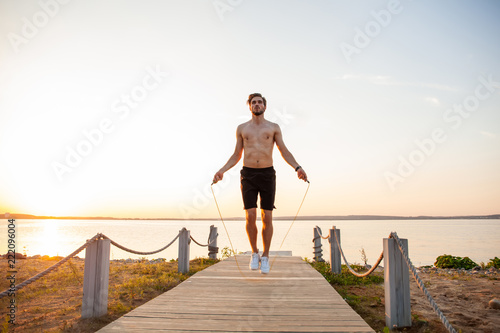 Portrait of muscular young man exercising with jumping rope