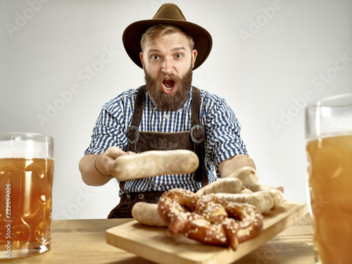Germany, Bavaria, Upper Bavaria. The young smiling man with beer dressed in traditional Austrian or Bavarian costume in hat holding mug of beer at studio