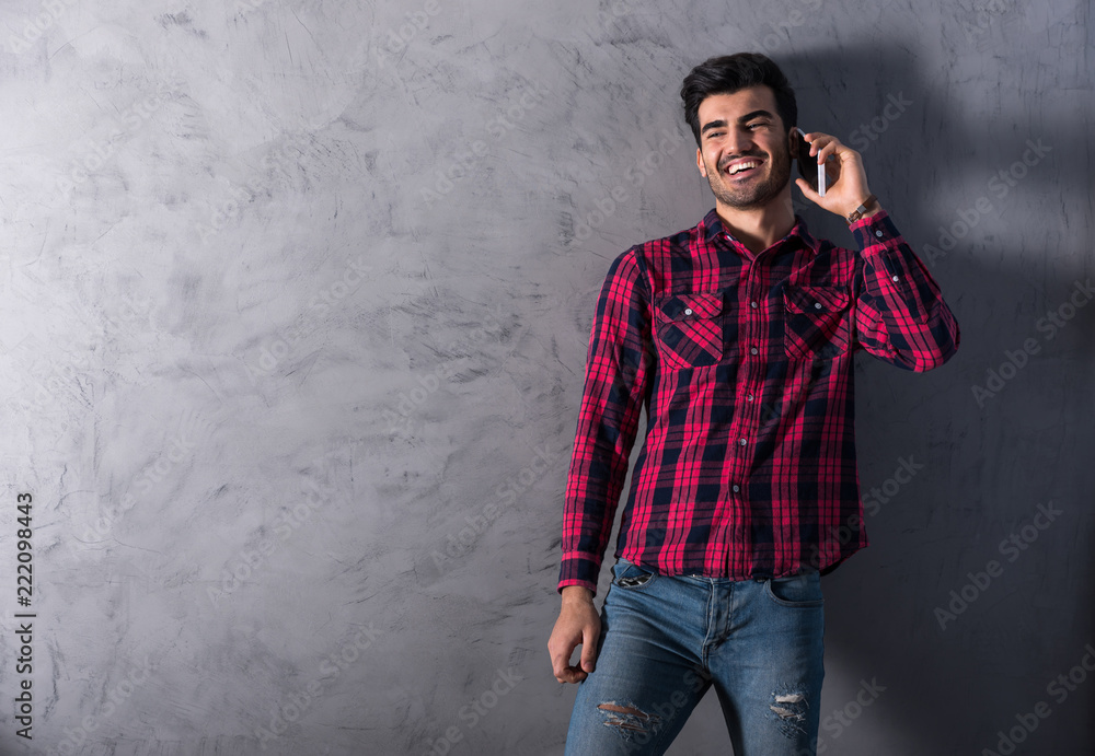 A happy handsome young man in a red checkered shirt talking on his phone in front of a grey wall in a studio. A happy handsome young man in a red checkered shirt talking on his phone in front of a grey wall in a studio.