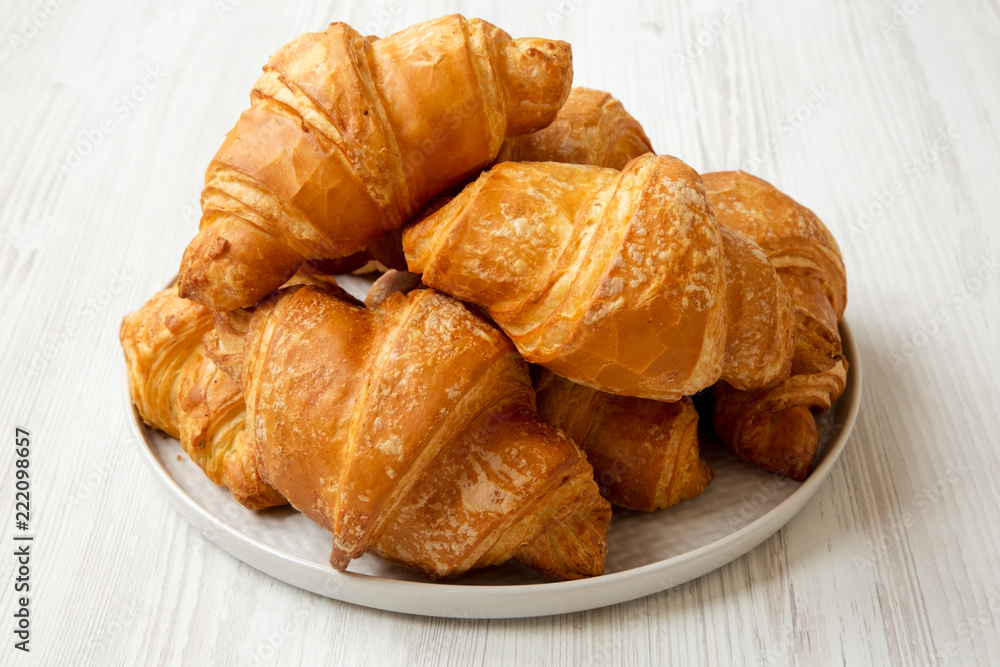 Fresh croissants on grey round plate on white wooden table, side view.