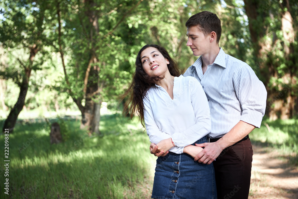 Fototapeta premium young couple walking in the forest, summer nature, bright sunlight, shadows and green leaves, romantic feelings