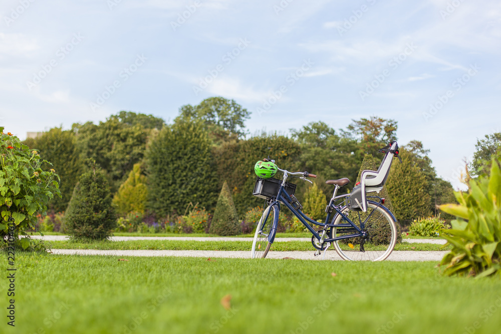 Obraz premium Vintage bicycle standing in Park with modern child bicycle carrier seat. Retro Fahrrad mit modernem Kindersitz und Fahrradhelm steht im Park.