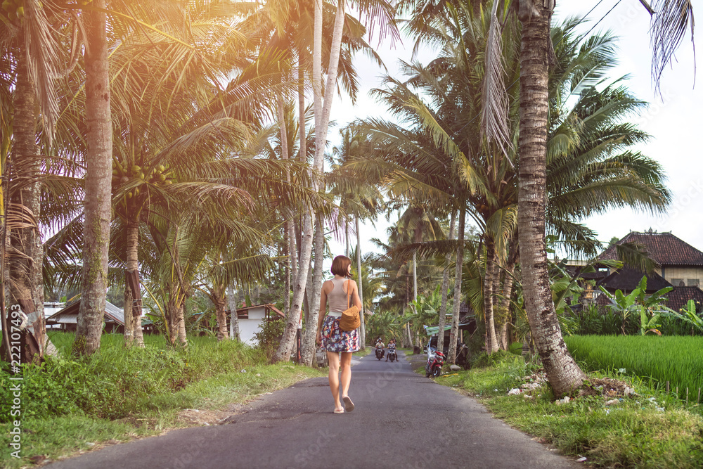 The girl walking down the road surrounded by palm trees. Bali island.